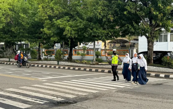 Pejalan kaki menyeberang di zebra cross dengan marka putih di jalan perkotaan