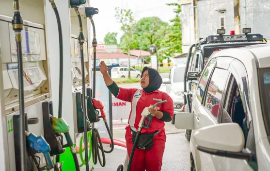 Pom bensin dengan papan harga BBM dan kendaraan di area pengisian