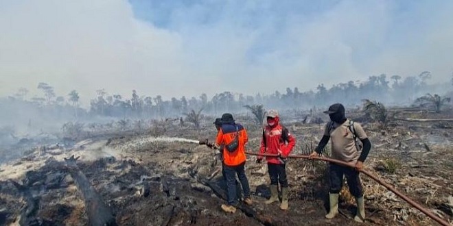 Petugas memadamkan kebakaran lahan di Aceh dengan asap di latar belakang