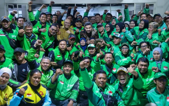 Pengemudi ojek online menunggu pesanan di pinggir jalan sambil memegang helm