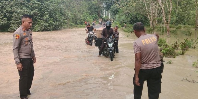 Personel Polsek Bosar Maligas membantu warga melintasi genangan banjir